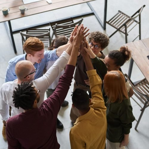 A diverse group of professionals high-fiving in a modern office, showcasing teamwork and collaboration.